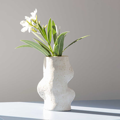 jarrón de cerámica artesanal blanco con flores en superficie neutra